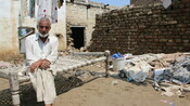 Rustam Khan sits in front of his destroyed house