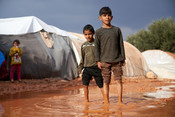 Brothers Jamal* (7), left, and Qasim* (10), right, walk through the mud in Zaitoun Maarshurin refugee camp